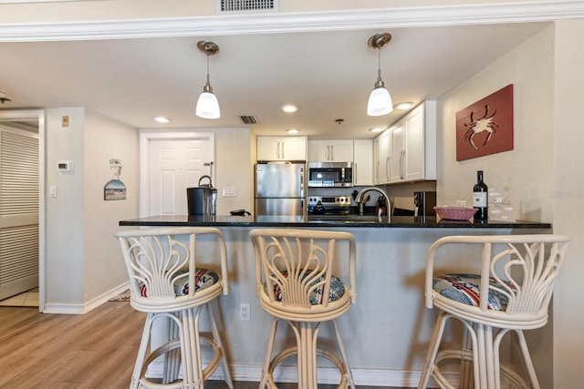 kitchen with a breakfast bar, appliances with stainless steel finishes, kitchen peninsula, pendant lighting, and white cabinets