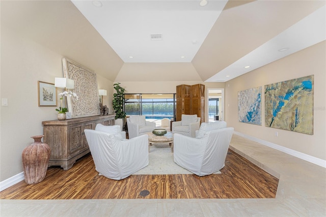 living room featuring lofted ceiling, a raised ceiling, and light wood-type flooring