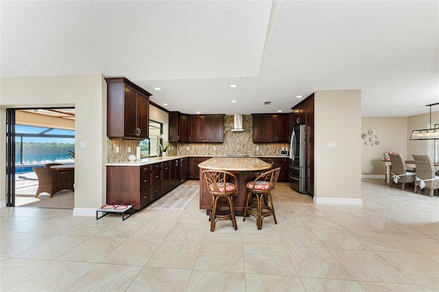 kitchen featuring decorative backsplash, stainless steel fridge, a center island, and a water view