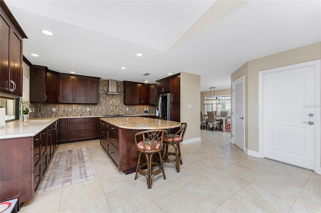 kitchen with wall chimney exhaust hood, sink, a center island, stainless steel fridge, and decorative backsplash