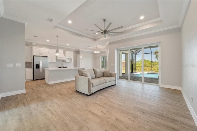 unfurnished living room featuring ornamental molding, ceiling fan, light wood-type flooring, and a tray ceiling