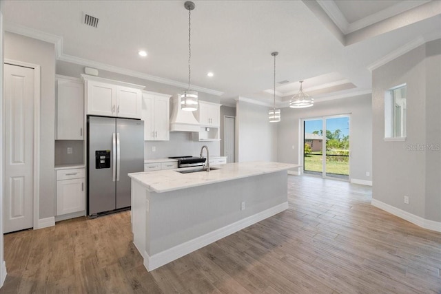 kitchen with sink, white cabinetry, stainless steel refrigerator with ice dispenser, light stone countertops, and a center island with sink