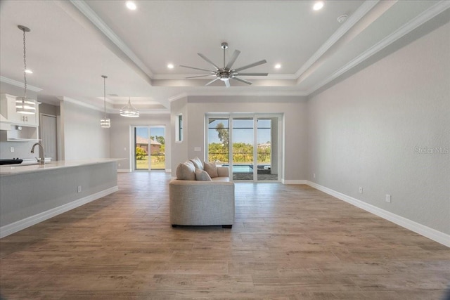 unfurnished living room featuring crown molding, sink, hardwood / wood-style flooring, and a raised ceiling