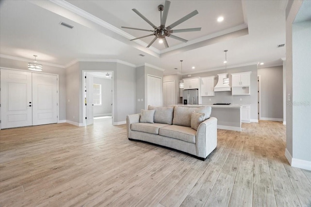 living room featuring ceiling fan, ornamental molding, a tray ceiling, and light wood-type flooring