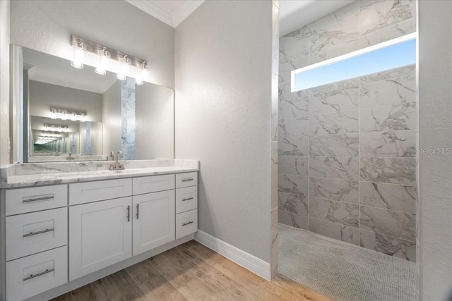 bathroom featuring tiled shower, ornamental molding, wood-type flooring, and vanity