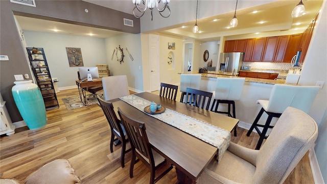 dining space with light hardwood / wood-style floors, a raised ceiling, and a chandelier