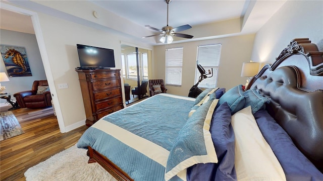 bedroom with dark hardwood / wood-style flooring, a tray ceiling, and ceiling fan