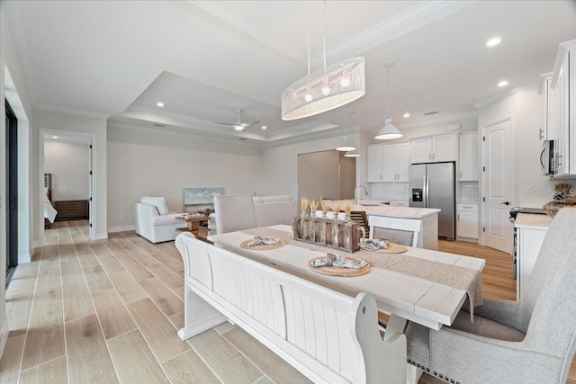 dining space featuring a raised ceiling, ornamental molding, sink, and ceiling fan