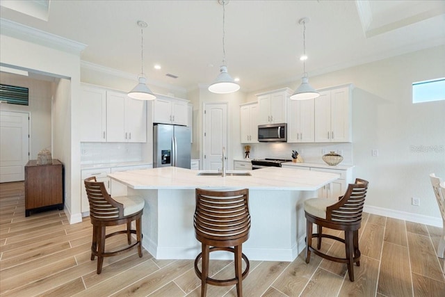 kitchen featuring sink, hanging light fixtures, stainless steel appliances, a kitchen island with sink, and white cabinets