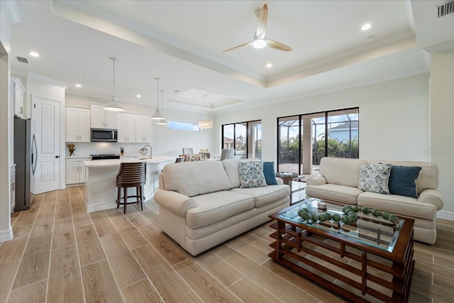 living room featuring crown molding, a raised ceiling, and ceiling fan