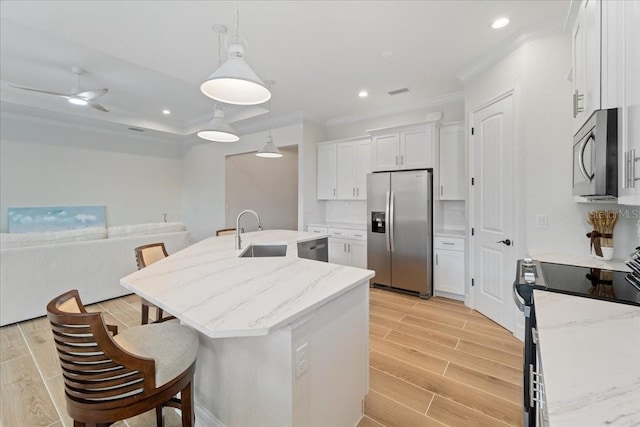 kitchen with appliances with stainless steel finishes, sink, white cabinets, hanging light fixtures, and a kitchen island with sink