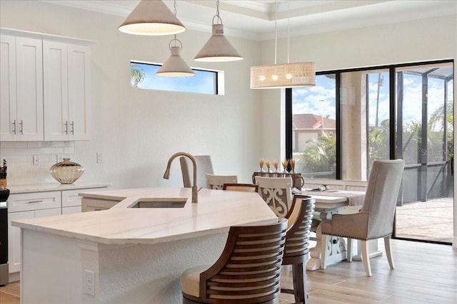 kitchen with sink, hanging light fixtures, light stone counters, white cabinets, and a center island with sink