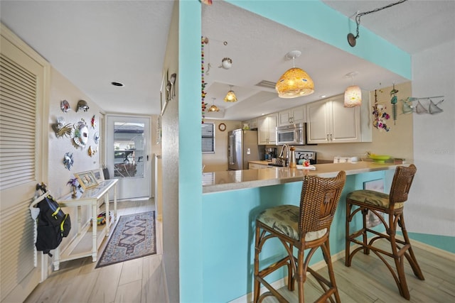 kitchen featuring a kitchen bar, hanging light fixtures, kitchen peninsula, stainless steel appliances, and light wood-type flooring