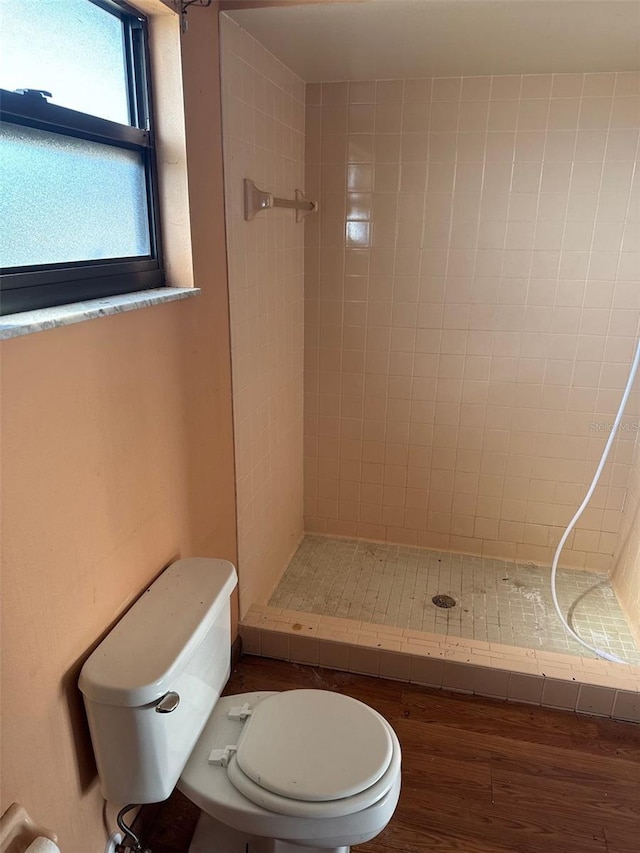 bathroom with wood-type flooring, toilet, and a tile shower