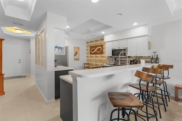 kitchen with a kitchen bar, light tile patterned floors, kitchen peninsula, stainless steel appliances, and white cabinets