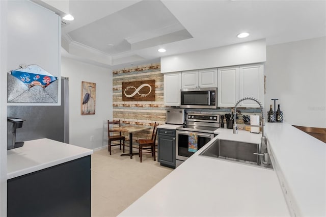 kitchen with appliances with stainless steel finishes, wood walls, sink, ornamental molding, and a raised ceiling