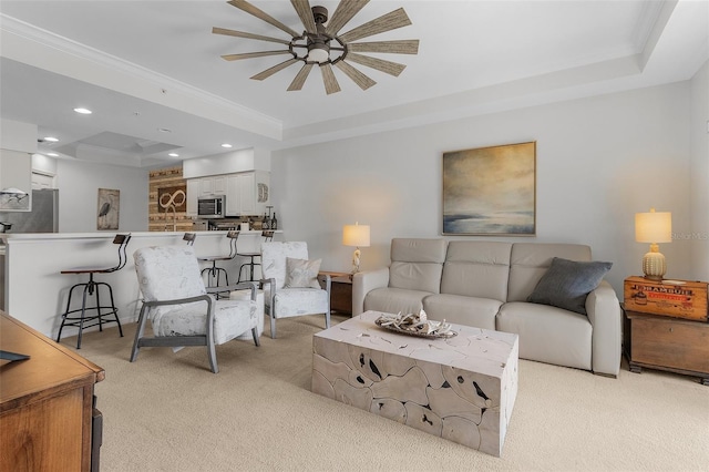 living room with ceiling fan, light colored carpet, ornamental molding, and a raised ceiling