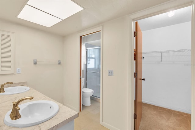 bathroom with a skylight, vanity, toilet, and a shower with shower door