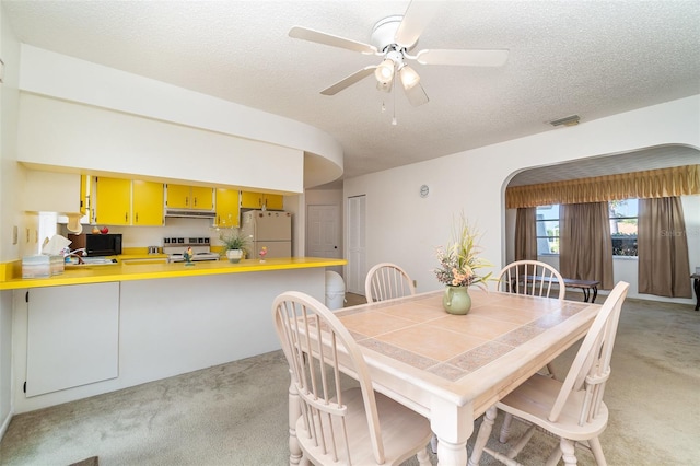 dining space with a textured ceiling, light carpet, and ceiling fan