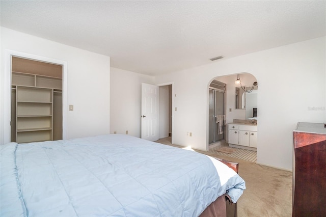 carpeted bedroom with ensuite bathroom, a closet, a spacious closet, and a textured ceiling