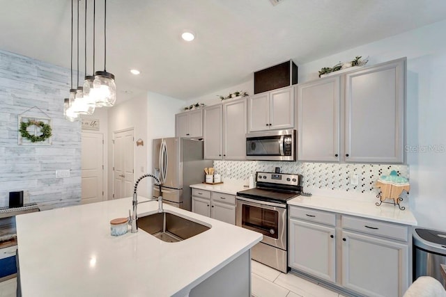 kitchen with appliances with stainless steel finishes, pendant lighting, sink, backsplash, and a kitchen island with sink