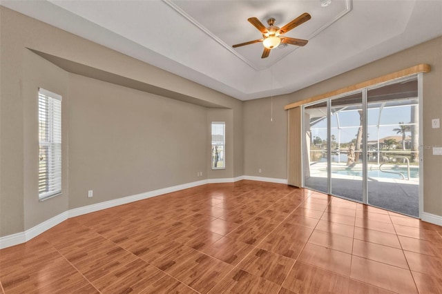 empty room with a tray ceiling, a ceiling fan, and baseboards