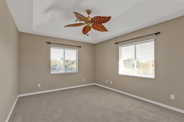 empty room featuring ceiling fan, carpet flooring, a raised ceiling, and baseboards