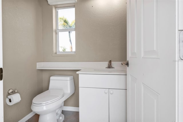 half bathroom featuring baseboards, toilet, and vanity