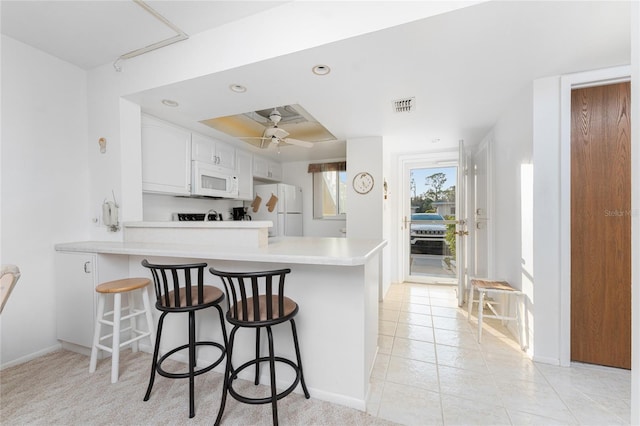 kitchen with white appliances, kitchen peninsula, a breakfast bar area, and white cabinets