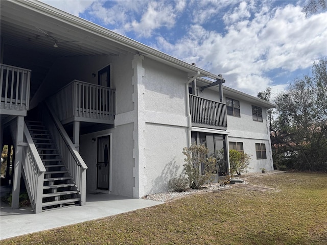 view of side of home featuring a yard, stairway, a balcony, and stucco siding