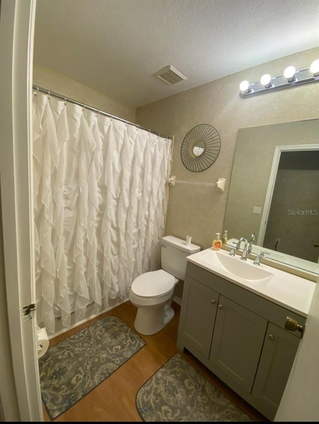 bathroom with visible vents, toilet, wood finished floors, a textured ceiling, and vanity