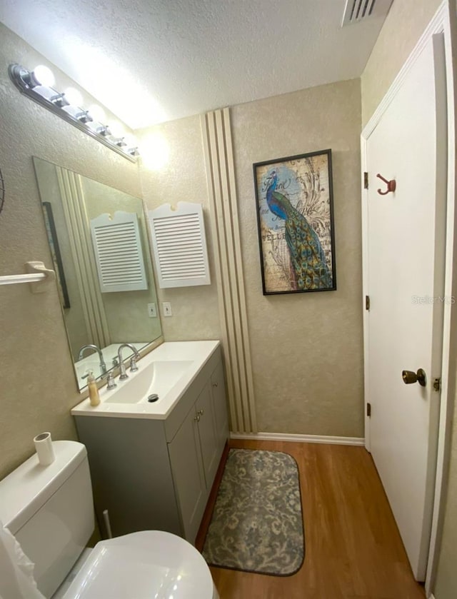 bathroom featuring a textured ceiling, toilet, wood finished floors, visible vents, and vanity