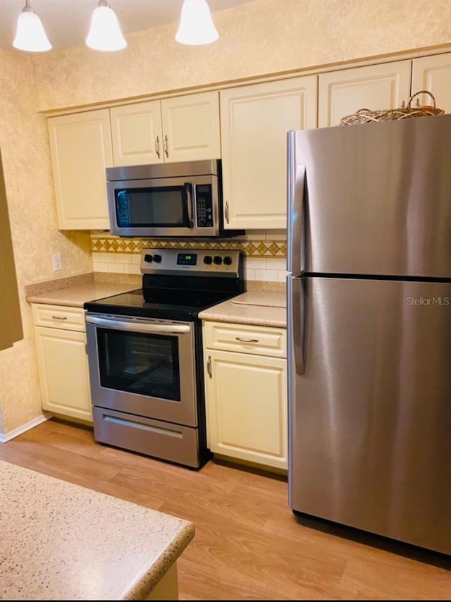 kitchen with tasteful backsplash, appliances with stainless steel finishes, light countertops, light wood-type flooring, and pendant lighting