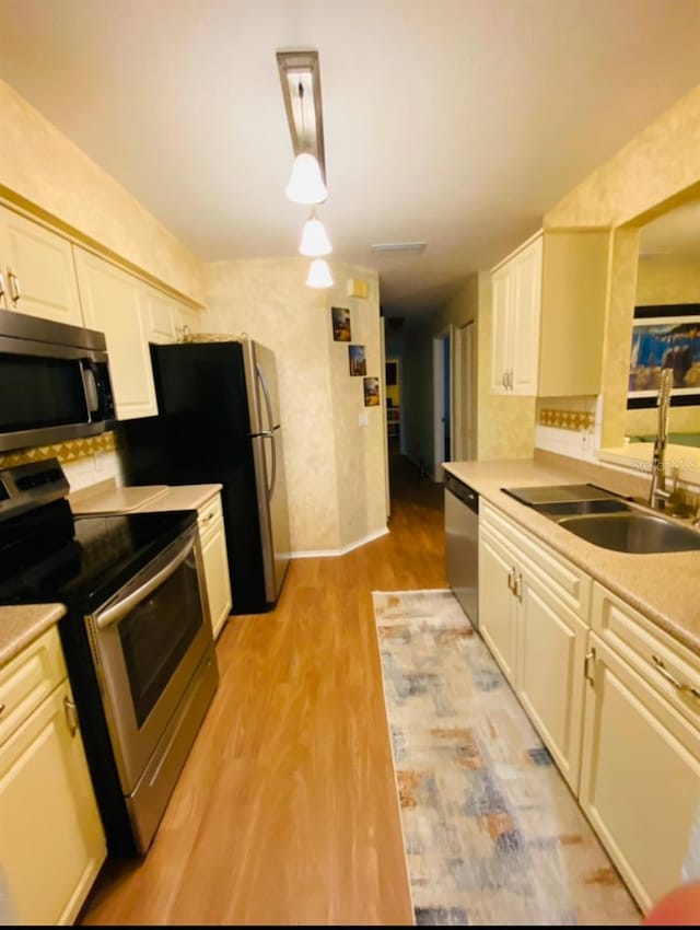 kitchen featuring sink, light hardwood / wood-style flooring, stainless steel appliances, decorative backsplash, and decorative light fixtures