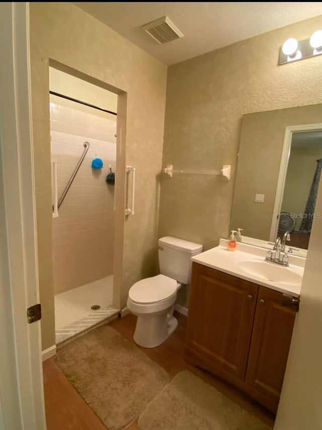 bathroom with a tile shower, vanity, hardwood / wood-style flooring, and toilet