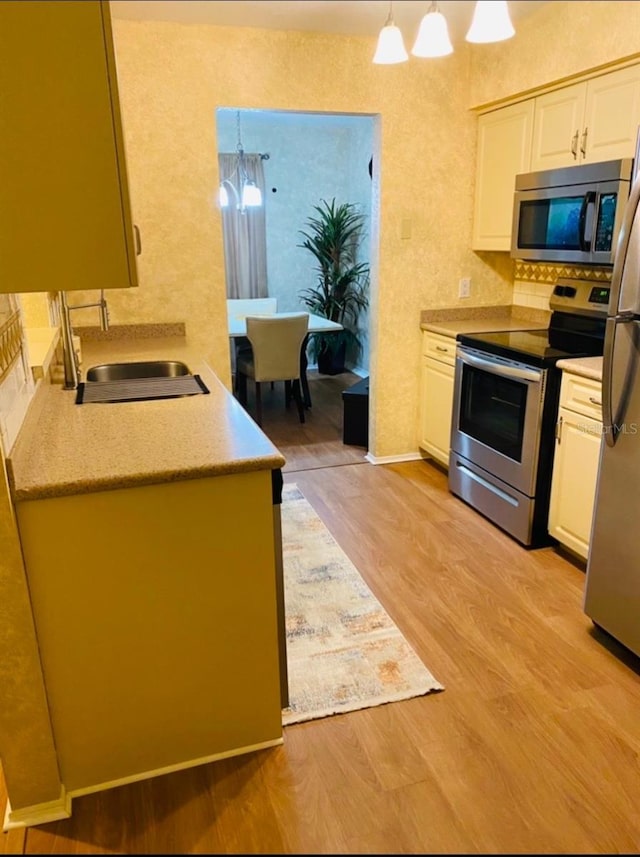 kitchen featuring sink, light hardwood / wood-style flooring, appliances with stainless steel finishes, white cabinetry, and decorative light fixtures