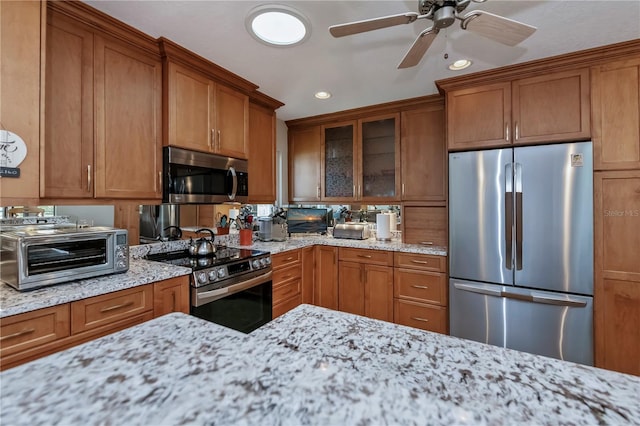 kitchen with light stone countertops, stainless steel appliances, and ceiling fan