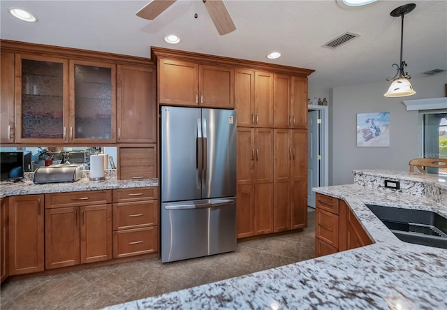 kitchen with decorative light fixtures, sink, stainless steel fridge, ceiling fan, and light stone counters