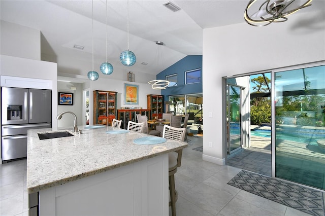 kitchen featuring hanging light fixtures, stainless steel refrigerator with ice dispenser, sink, and light stone counters