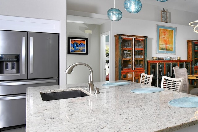 kitchen featuring pendant lighting, sink, light stone counters, and stainless steel refrigerator with ice dispenser