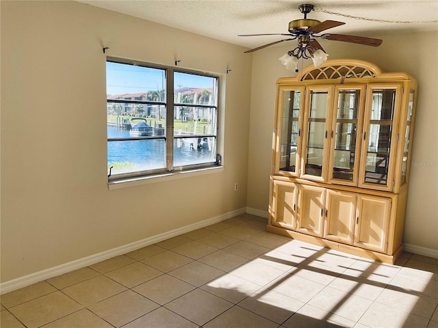 tiled empty room featuring ceiling fan, a textured ceiling, and a water view