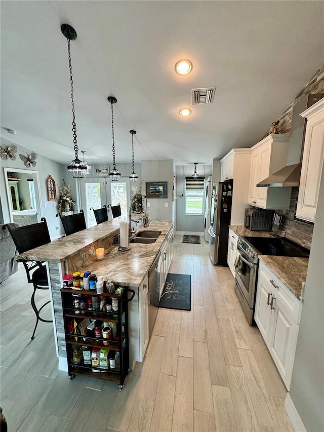 kitchen featuring pendant lighting, a kitchen island with sink, stainless steel appliances, white cabinets, and a kitchen bar