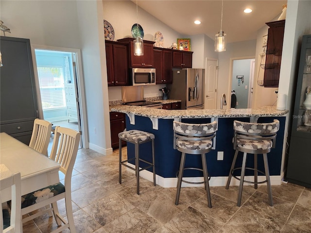 kitchen with lofted ceiling, a kitchen bar, decorative light fixtures, stainless steel appliances, and light stone countertops