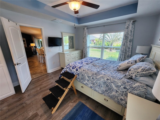 bedroom with dark hardwood / wood-style floors, ceiling fan, and a tray ceiling