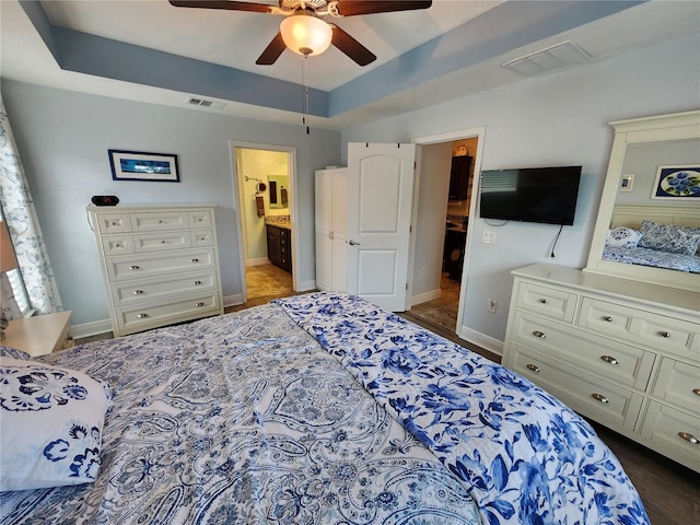 bedroom with ensuite bath, a raised ceiling, and ceiling fan