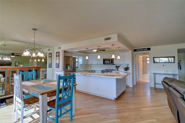 dining area featuring a raised ceiling, ceiling fan, and light wood-type flooring