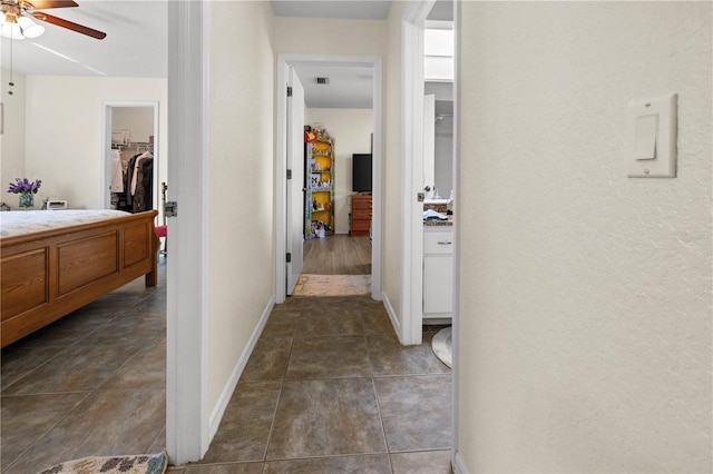 corridor featuring visible vents, baseboards, and dark tile patterned flooring