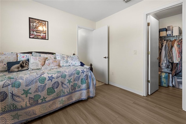 bedroom with a walk in closet, wood-type flooring, and a closet