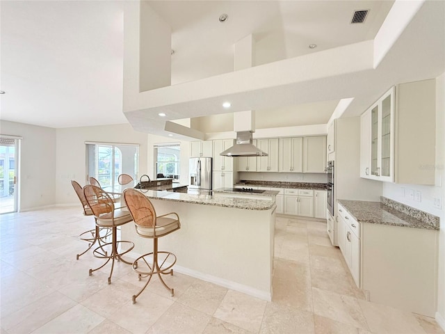 kitchen with light stone countertops, stainless steel appliances, white cabinets, and a center island with sink