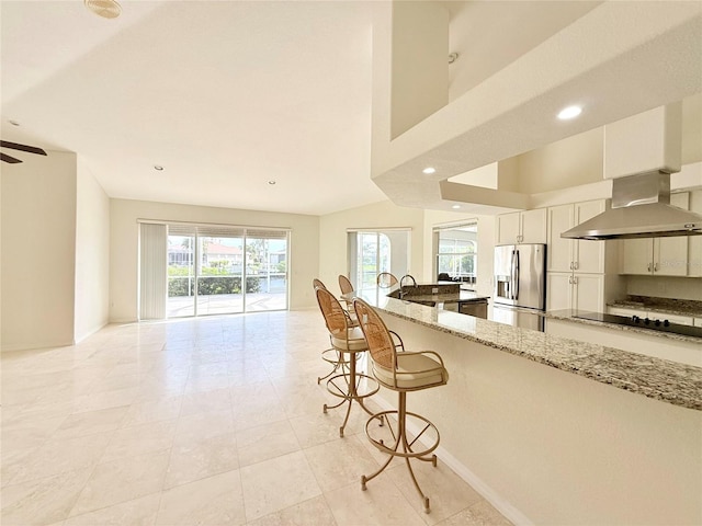 kitchen with stainless steel refrigerator with ice dispenser, a kitchen bar, extractor fan, white cabinetry, and light stone countertops